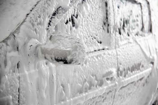 Closeup view of motor car with solid layer of soap sud during car wash. Selective focus with shallow depth of field,