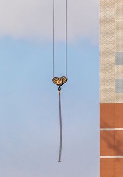 Construction site. Unfinished apartment building. Special industrial crane hook on chains in the middle. Blue sky background.