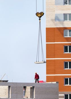 Construction site in Russia. Concrete panel being lifted by a crane. Unfinished apartment buildings. Construction worker wearing a hard hat.