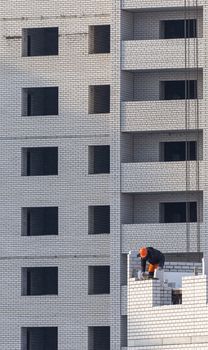 Construction site. Unfinished apartment building. Construction workers dressed in special clothing laying bricks