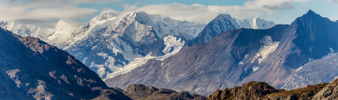 Beautiful panorama of massive mountains and snowy peaks covered with white clouds. Glacier Bay National Park. Alaska, USA