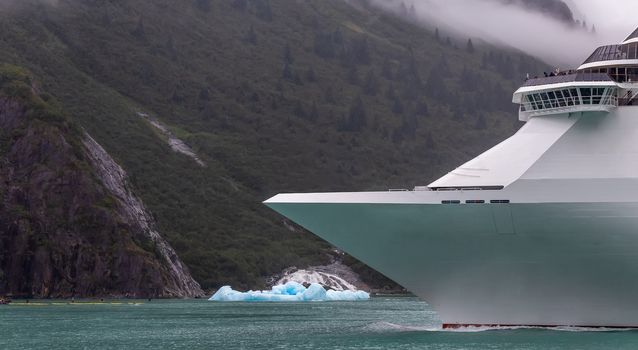 Cruise ship sailing in Alaska among icebergs. Ship's bow with mountains and cloud in the background.