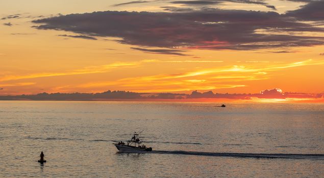 Fishing boat sailing at sunset in Mexico. Beautiful orange sky and a tiny boat silhouette in the background.