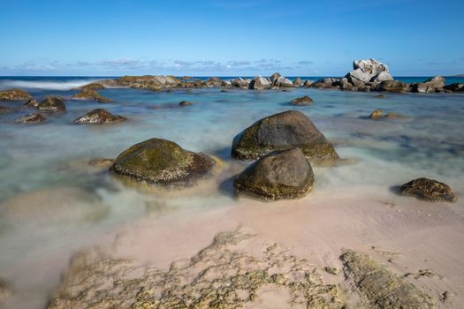 Beautiful rocky beach in Aruba. Three big stones in the foreground. Waves, sky and clouds in the background. Long exposure.