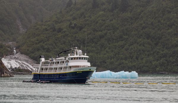 Tracy Arm Fjord, Alaska, US - August 23, 2018: National Geographic's Sea Bird vessel drifting with a mountain, a waterfall, and an iceberg behind it in Tracy Arm Fjord in Alaska, USA