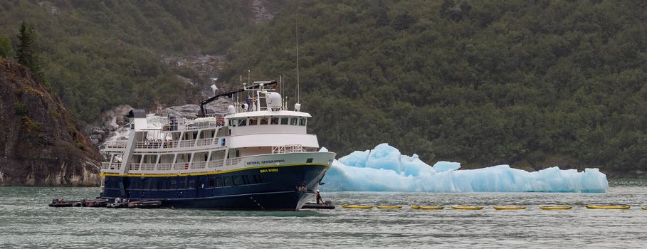 Tracy Arm Fjord, Alaska, US - August 23, 2018: National Geographic's Sea Bird vessel drifting by an iceberg with some personnel in a small boat next to it. Close view.