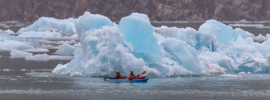 Tracy Arm Fjord, Alaska, US - August 23, 2018: Two tourists sailing in a kayak among huge icebergs in Alaska, USA