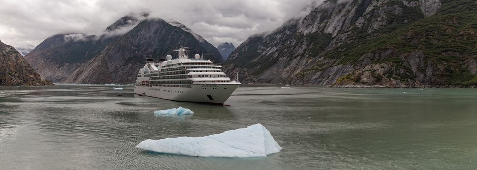 Tracy Arm Fjord, Alaska, USA - August 23, 2018: Panorama of Seabourn Sojourn cruise ship drifting with a huge iceberg floating in the foreground