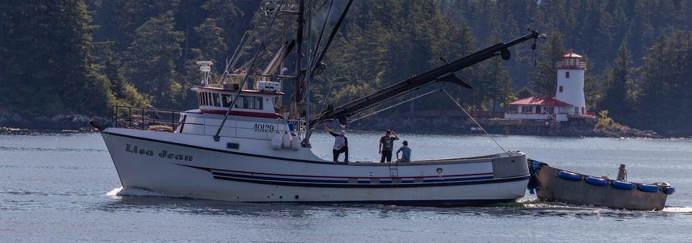 Sitka, Alaska, USA - September 10, 2018: Fishing boat Lisa Jean sailing in marina. Lighthouse and forest in soft focus in the background. Sitka, Alaska, USA