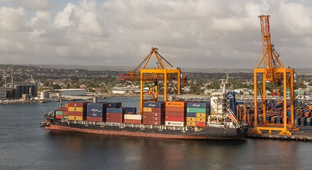 Bridgetown port, Barbados, West Indies - May 2, 2020: Bridgetown port with loading cranes and cargo ship being loaded with containers