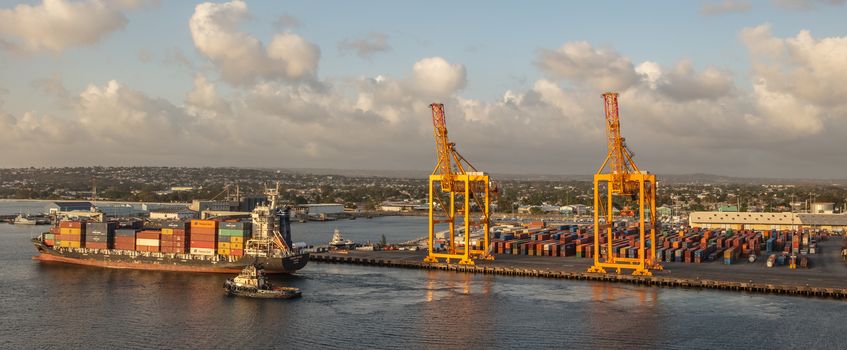 Bridgetown port, Barbados, West Indies - May 2, 2020: Bridgetown port with loading cranes and full cargo ship sailing away