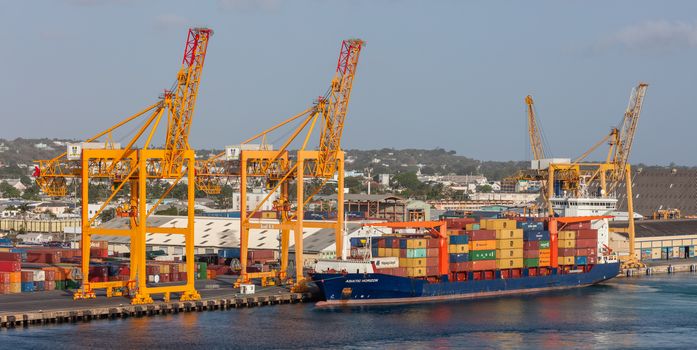 Bridgetown port, Barbados, West Indies - May 16, 2020: Bridgetown port with loading cranes and cargo ship being loaded with containers