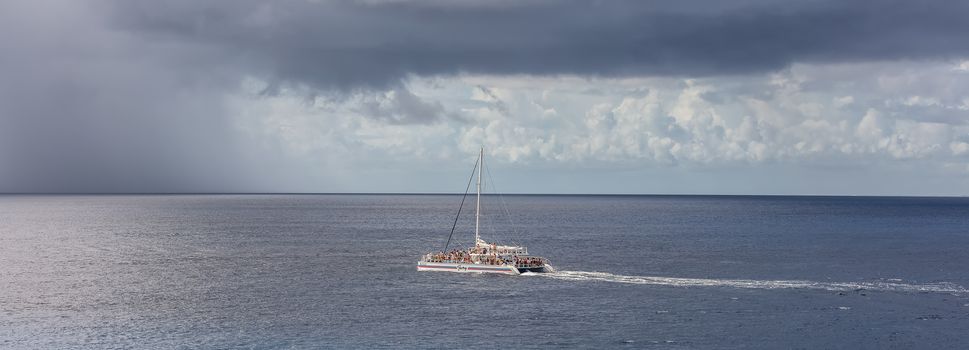 Cozumel, Mexico - December 17, 2019: Catamaran Fury sailing by the island of Cozumel in Mexico. Catamaran full of tourists. Stormy weather in the background