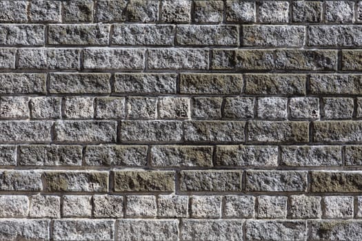 Brick wall made of grey and dirty white bricks. Front view.
