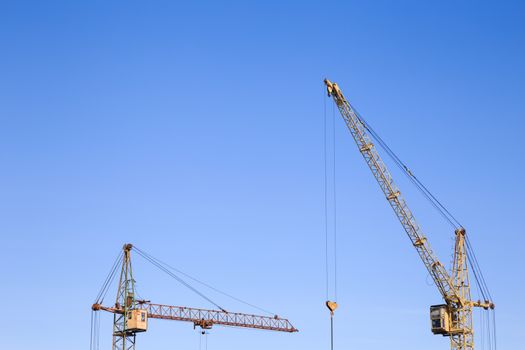Front distant view of two cranes on a light blue sky background. Construction site