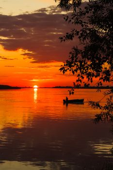 Beautiful sunset at a river with a boat sailing on it. Orange colors reflecting in the water.