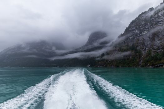 View on water waves produced by a sailing boat and mountains covered with clouds in the background