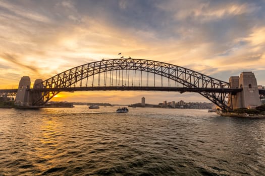 View of Sydney harbor bridge at sunset and a boat sailing under it in the background