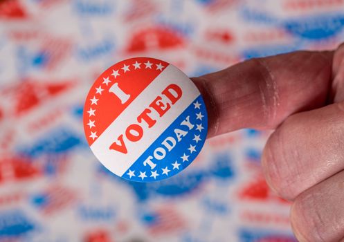 Finger with I Voted Today button in front of many voting stickers given to US voters in Presidential election to illustrate vote rights