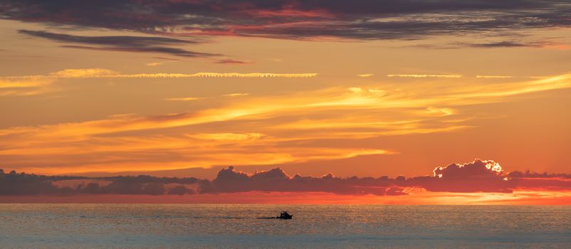 Beautiful orange-and-yellow sunset with a tiny boat sailing off the coast of Cozumel island in Mexico