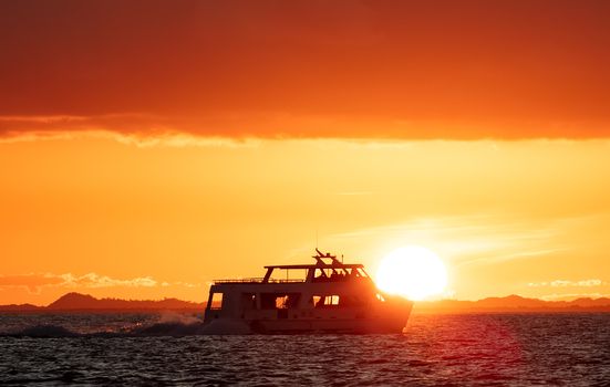 Boat sailing by the coast of Belize with sun setting down in the background and lighting up the sky