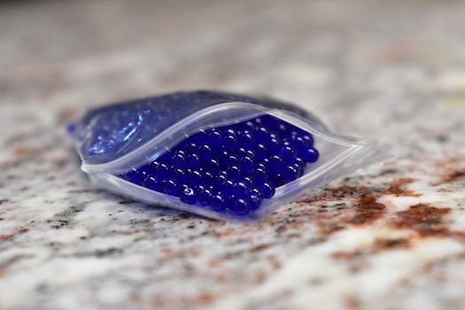 Tiny Blue Orbs in a Plastic Pouch on a Granite Countertop