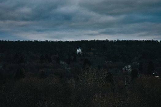 A Lone Church Building With a Blue Roof on a Mountain Covered in Dead Trees With a Cloudy Sky