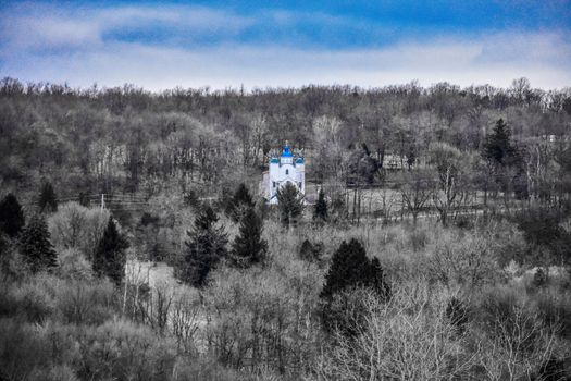 A Lone Church Building With a Blue Roof on a Mountain Covered in Dead Trees With a Cloudy Sky