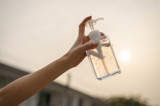 Hand with antibacterial transparent hand sanitizer gel in a plastic bottle.