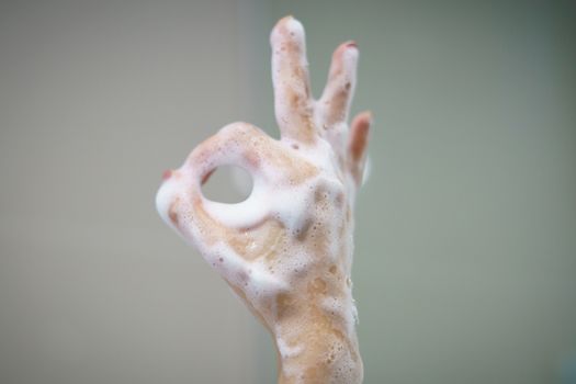 Hand with soft foam bubble from soap is showing ok sign.