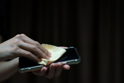 Hand holding and cleaning mobile phone screen with a napkin for corona virus or Covid-19 protection.