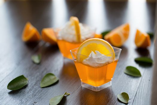 Orange jelly in a cup with whipped cream and orange sliced on black wooden background.