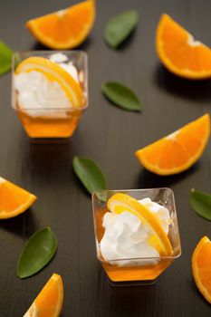 Orange jelly in a cup with whipped cream and orange sliced on black wooden background.