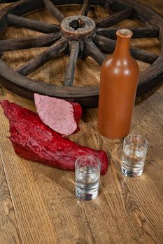 Ham sausage, ceramic bottle and glasses of vodka on a wooden desk