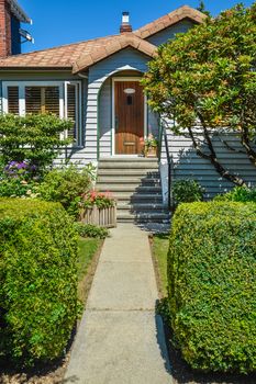 Concrete pathway to residential house entrance via landscaped front yard with hedgerows by sides