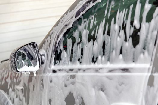 Closeup view of motor car window with layer of soap sud during car wash. Selective focus with shallow depth of field,