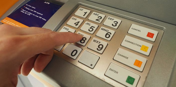 ATM machine and close-up man hand pushing on the pin number button to withdraw the money credit. 