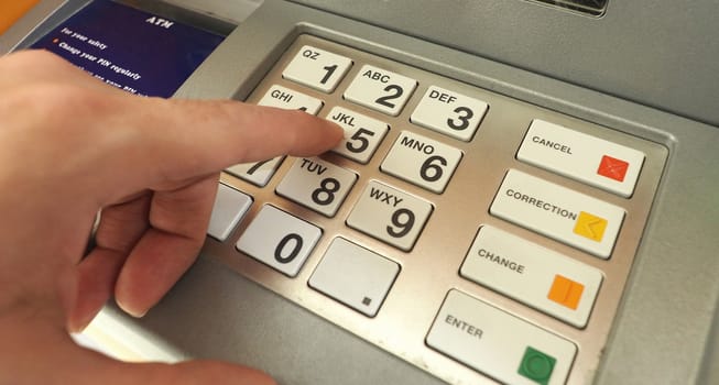 ATM machine and close-up man hand pushing on the pin number button to withdraw the money credit. 