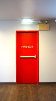 Emergency fire exit door and red color and white wall in building.