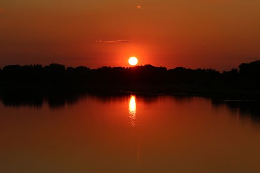 A great sunset with a lake view and bushes and trees in the background