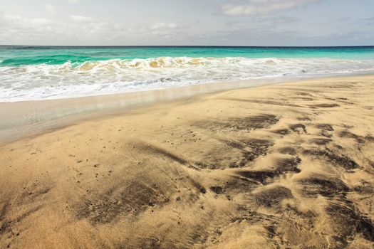 Gorgeous empty beach with golden and black volcanic spots sand, with azure sea in the background. Sal, Cape Verde