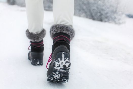 Detail of woman lifting her black and gray snow boot with faux fur and purple laces, showing tread of the boots, shot on winter overcast day.