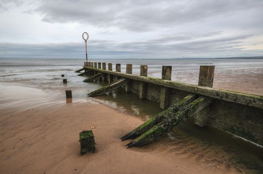 Old wood and stone groyne structure covered with green algae on Portobello beach in low tide with North sea in the backgroud shot on overcast day. Edinburgh, Scotland.