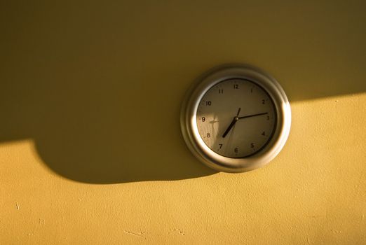 Analogue clock on the yellow wall showing 7:14 time, light from the side, long shadows emphasising early morning sun.