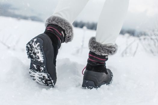 Detail on sole of black winter shoes with purple details, worn by girl walking in snowy country in winter.