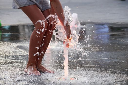 barefoot girl touching the fountain on the sidewalk in the evening