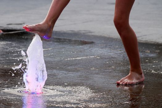 barefoot girl touching the fountain on the sidewalk in the evening