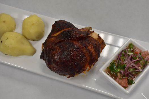 Rotisserie Chicken on a White Plate on a White Table With Potatoes and a Small Salad Next to It