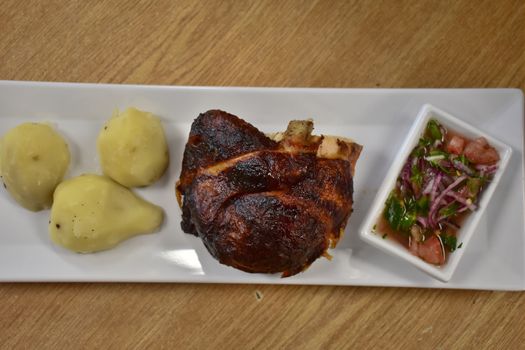 Rotisserie Chicken on a White Plate on a Wooden Table With Potatoes and a Small Salad Next to It