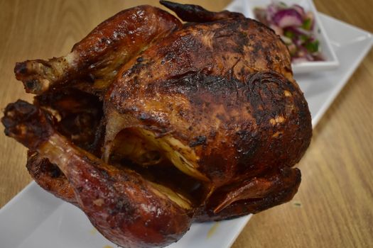 Rotisserie Chicken on a White Plate on a Wooden Table With Potatoes and a Small Salad Next to It